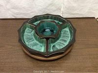 Top view of four-piece ceramic serving set fitted on wooden rotating base. Green ceramic with dark edges.