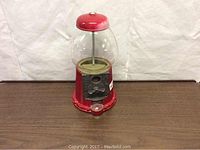 Front view of vintage red metal and glass gumball vending machine with coin slot and turn handle