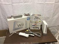 Photo of Nintendo Wii console, original box, power adapter, AV cable, Wii Remote controller, sensor bar, and 18 Wii game cases stacked