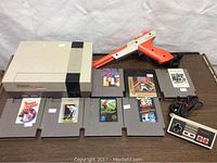 Photo showing the Nintendo NES console, NES Zapper, NES controller, and seven game cartridges laid out on a table.
