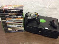 Photo of the Xbox console, controller, power cable, and 15 Xbox game cases stacked on a table.