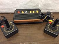 Atari Flashback 2 console with two classic joystick controllers and power cord on wood table.