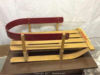 Front angle of the Baby Bob wooden sled showing the red curved backrest, wooden slats for seating, and base runners on a wooden table.