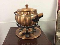 Front view of large copper soup tureen placed on matching copper tray, showing wooden side handles and iron stand.
