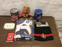 View of full lot including stuffed bear in Calgary Flames jersey, wrapped scarf, hat with tag, two beer coolers, coin holder, and playing cards