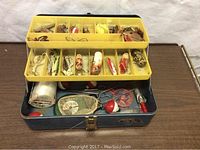 Open metal tackle box filled with assorted vintage fishing lures and tackle