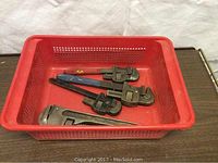 Four pipe wrenches of various sizes in a red basket, showing their overall length and condition.