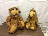 Photo showing two vintage ALF stuffed toys, one larger with a talking feature and one smaller. Both have brown shaggy fur and lighter brown faces and limbs.