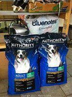 Two new sealed 34-pound bags of Authority Experts in Nutrition adult dog food with lamb & rice formula. Blue packaging showing a happy dog.
