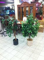 Two artificial potted plants side by side on tiled floor, one in black pot with variegated leaves and one in white woven pot with green leaves