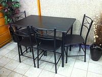Black rectangular table viewed from a corner angle with four matching black metal frame chairs around it, showing the condition and design of the table and chairs.