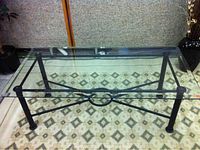 Complete view of the rectangular glass top coffee table showing black metal frame, decorative crossbars, and clear glass surface.