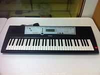 Front view of Yamaha Portable Grand keyboard showing full 61 keys and control panel with LCD display and buttons.