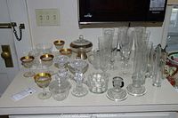 Photo shows entire collection of glassware on counter including gold rimmed glasses, clear stemmed glasses, compote with lid, and candle holders.