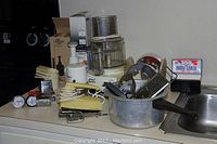 Overview of kitchen items including a Cuisinart food processor, hand mixer, cheese graters, utensils, and measuring cups on a kitchen counter beside a sink.