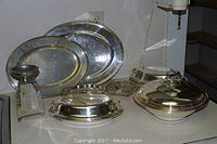 Grouped pewter and silverplate trays and covered bowls on countertop, varying sizes and shapes visible