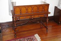 Full front view of flip-top desk showing closed top, carved arch panels and turned legs.