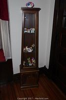 Full view of tall wood curio cabinet with glass front and display shelves inside, showing assorted collectibles on shelves.