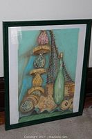 Framed still life art featuring sea-themed objects including decorative glass floats and a green bottle with fishing net in green frame.