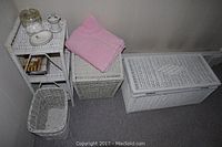 Full view of the set with hamper, chest, waste basket, and small stand with pink towel on top.