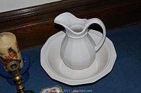 White ceramic pitcher and basin set placed on the floor against a wooden baseboard