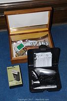 Electric shavers and wooden cigar humidor placed on blue carpet. Sanyo electric shaver box visible along with another shaver and black carrying case.