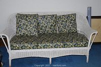 Full view of white wicker sofa with floral cushions on a blue carpet.