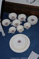 Full view of the Wedgwood dinnerware set arranged on a blue surface including cups, saucers, and plates varying sizes showing floral design and embossed borders
