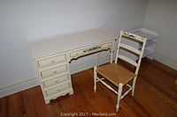 Full view of the off white laminate top desk with four drawers on the left and matching off white rushed seat chair placed beside it.