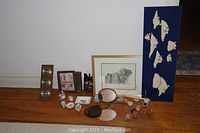 Full view of lot contents arranged on wooden baseboard and floor including barometer, ceramic ashtray, prints, trinket boxes, textile wall art, and mirror