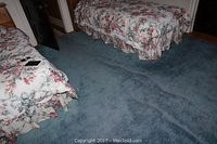 Blue area rug on floor between beds, showing wear and wrinkles