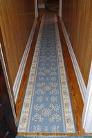 Full length view of blue floral patterned rug runner laid out in a narrow hallway with wood floor and white baseboards.