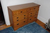 Front view of wood dresser with six drawers and metal handles on a blue carpet.