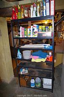 Full view of black metal shelving unit with partial cleaning bottles and cleaners, towels, cleaning items, and fluorescent bulbs.