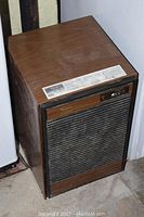 Front and side view of a vintage Whirlpool dehumidifier in woodgrain and black color scheme, showing the vented grille and control panel.