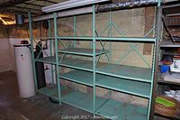 Full view of assembled green metal shelving unit in basement storage area, showing five shelves per section and cross braces on the back.