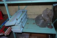 Stack of seven blue painted wood shutters with curtain fabric inserts on a metal shelf next to a wrapped lamp base