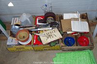 Three Pepsi and another wooden crate containing assorted items like plastic ashtrays, grill tools, Dolce Vita wall decor, paper items, and a plastic jug.