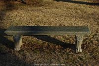 Full view of heavy concrete bench outdoor on grass, showing long textured seating surface and two thick carved legs with paw-like feet.