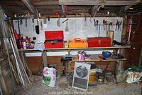 Full view of wooden shelves with boxes, hand tools, sticks, window fan, paint cans, and other workshop items.