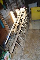 Photo showing two wooden ladders leaning against a wall in a storage area, one ladder longer than the other.