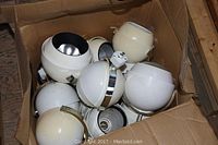 Box filled with multiple spherical white track lighting globes showing wear and pitting.