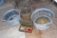 Photo showing both galvanized tubs, metal bucket, and open metal box with contents on wooden floor.