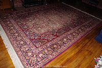 Full view of large red tone Karastan rug with floral designs laid on wood floor, showing wear and overall pattern.