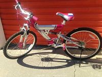 Side view of the Kent youth mountain bike showing silver and pink color scheme, front and rear tires, and 21-speed gear cassette.