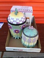 Two ceramic cookie jar canisters with floral patterns and a boxed Corelle tea kettle behind them.
