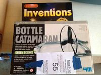 Photo showing the 4M Bottle Catamaran kit box with visible product name and details, alongside the Scholastic Inventions book.