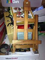 Small wooden easel standing upright in front of a cluttered area containing various art and craft items, visible stickers and a box underneath.