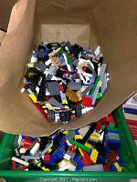 Cardboard box filled with loose assorted Lego pieces in multiple colors and sizes, including wheels and specialized bricks.