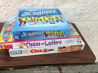 Stacked view of the game boxes Scrabble Junior, Clue Junior, and Chutes and Ladders on a wooden surface
